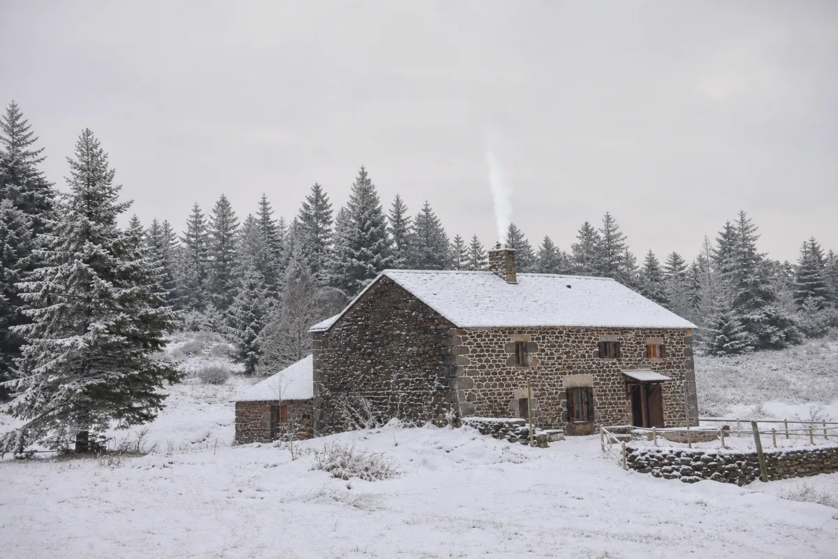 Gîte en pierre sous la neige sur le plateau ardéchois, fumée sortant de la cheminée