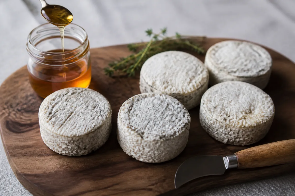 Fromages de chèvre picodon posés sur une planche en bois avec un couteau et du miel