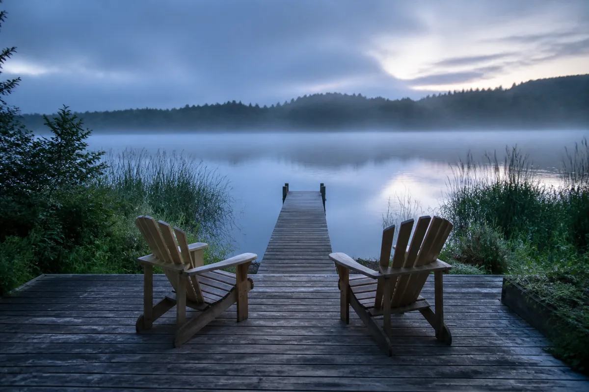Terrasse en bois face à un lac calme au petit matin avec brume légère sur l&rsquo;eau